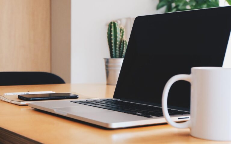 Kuvituskuva jossa on siistillä työpöydällä kannettava tietokone. puhelin, muistikirja ja kahvikuppi. Taustalla näkyy viherkasveja.