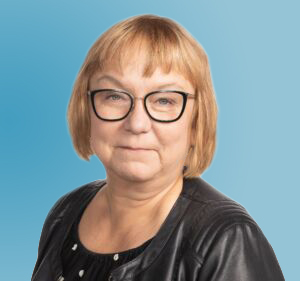 Vakavanhko silmälasipäinen nainen, jolla on polkkatukka, oo-aukkoinen pusero ja nahkatakki.